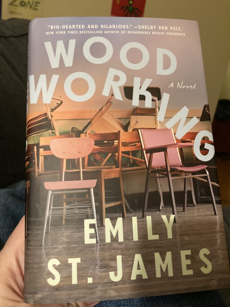 A hand holding a hardcover copy of the book Woodworking, by Emily St. James.